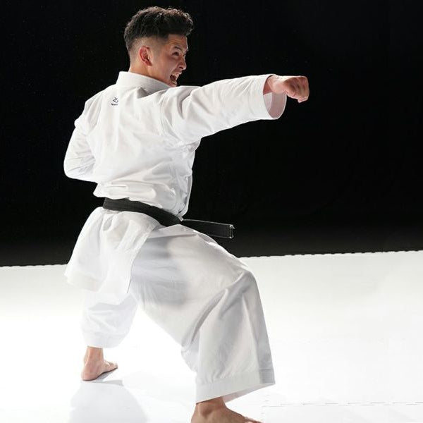 Person in a white martial arts uniform with a black belt performing a martial arts move on a black and white background.