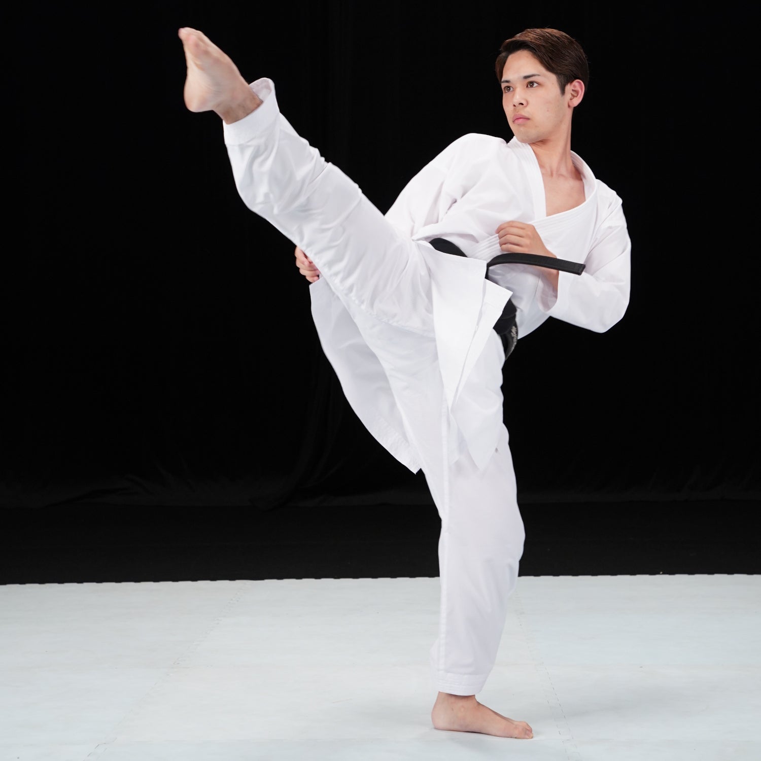 Person in a white martial arts uniform performing a high kick against a black background
