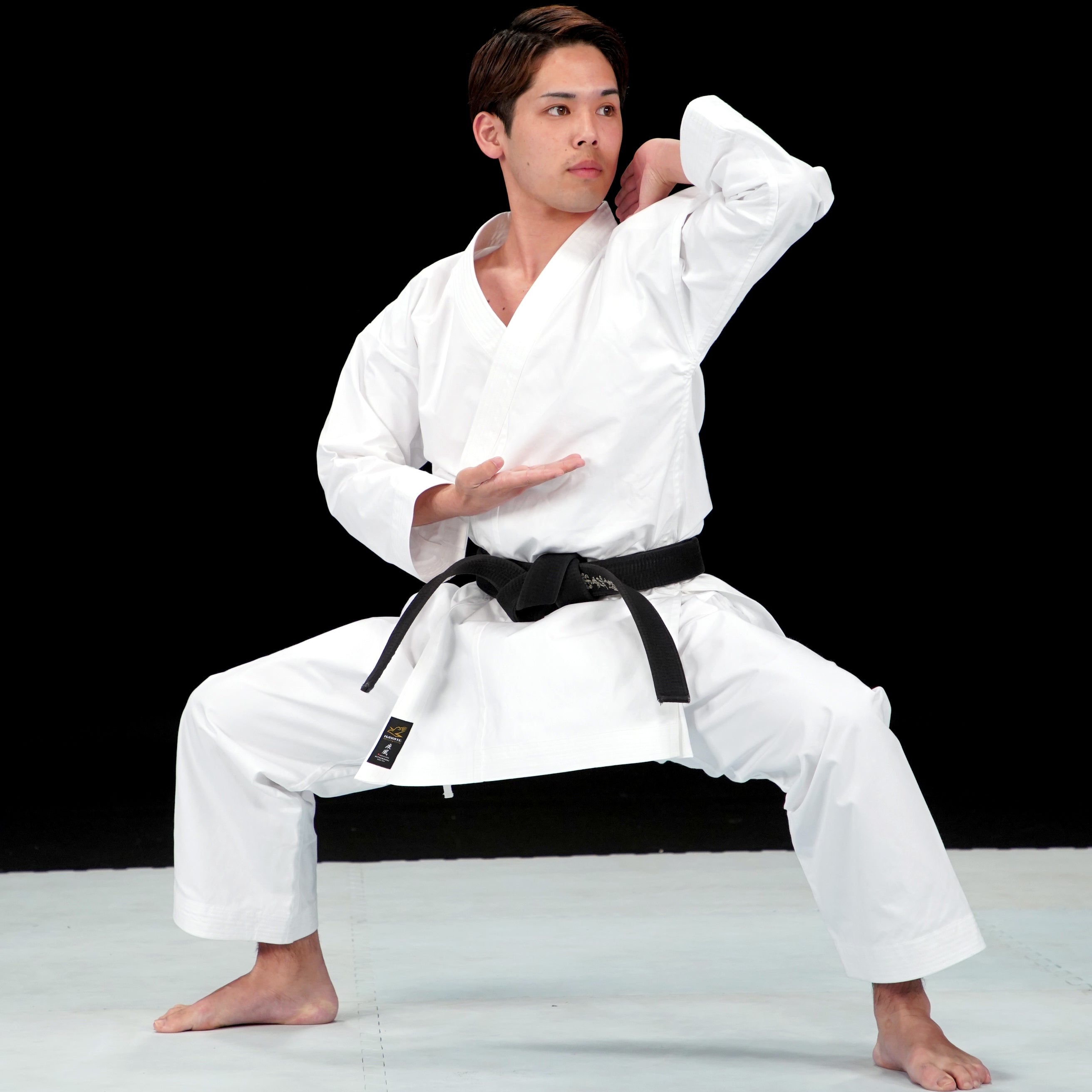 Person in a Hayate white martial arts uniform with a black belt posing against a black background