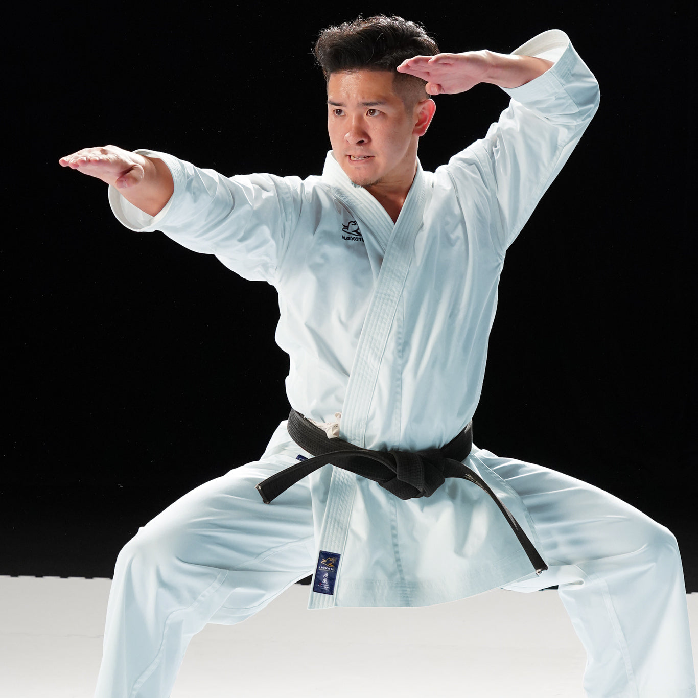 Person in a white martial arts uniform with a black belt posing against a black background